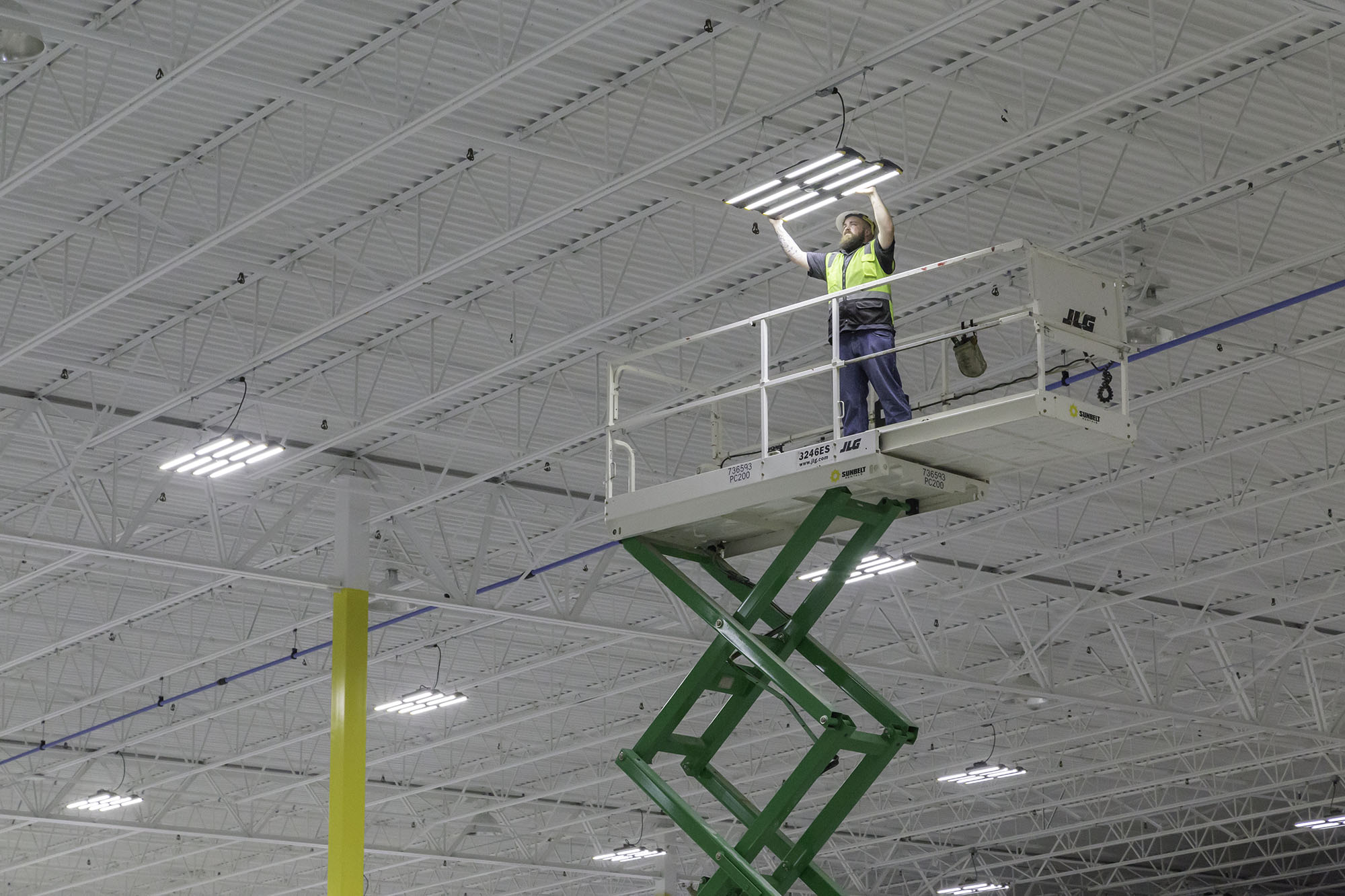 worker on scissors lift installed led lighting in manufacturing facility